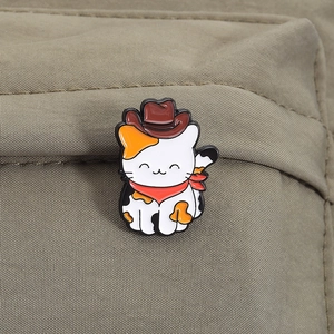 Détail d'un pin's en émail chat calicot avec un chapeau de cow-boy fixé sur tissu