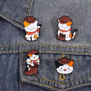 Detailed view of creative cat cowboy enamel pins pinned on a blue denim jacket pocket