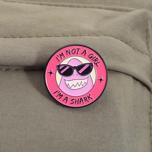 Pin's émaillé rose avec requin violet et texte I'M A SHARK sur un tissu kaki rustique
