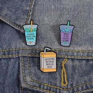 Detailed view of three drink-shaped enamel pins pinned on a blue denim jacket pocket