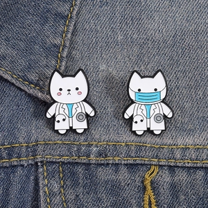 Close-up of enamel cat doctor brooches on denim fabric with stethoscope detail