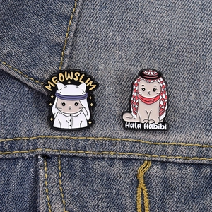 Detailed view of Meowslim and Hala Habibi enamel pins on blue denim fabric background