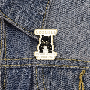Detail of funny black cat crochet enamel pin pinned on a blue denim jacket lapel