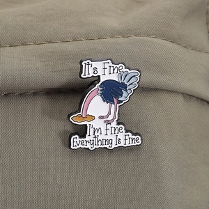 Nahaufnahme einer lustigen Straußen-Emaille-Anstecknadel mit dem Text 'It's Fine' auf Stoff