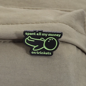 Gros plan d'un pin's en émail noir avec texte vert fluo sur un tissu vert olive