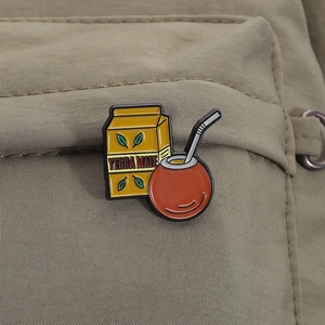 Close-up of yerba mate enamel pin with yellow container and teapot on canvas fabric