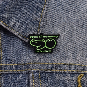 Pin's émaillé amusant avec texte Spent all my money on trinkets sur une veste en jean