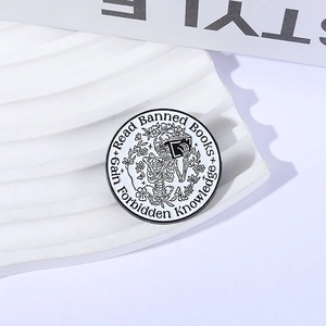 Minimalist round enamel pin with a skeleton reading books and floral pattern detail