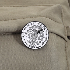 Macro detail of round enamel skull reading badge pinned on a khaki canvas backpack