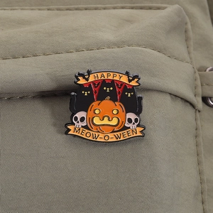Macro detail of Halloween enamel pin with black cats and pumpkin on green fabric