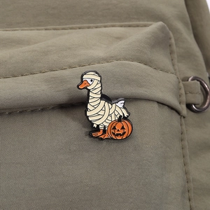 Detail of Halloween mummy goose enamel pin with pumpkin on green fabric background
