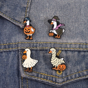 Detail of four Halloween duck enamel pins with pumpkin and ghost themes on denim fabric
