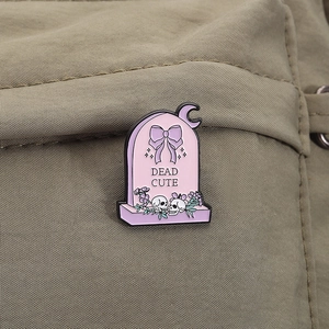 Close-up of Dead Cute tombstone enamel pin with bow and skulls on a canvas bag