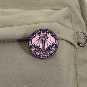 Détail d'un pin's en émail chauve-souris rose et lune sur une sangle de sac verte