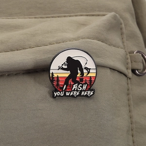 Détail du pin's émaillé Bigfoot qui pêche fixé sur un sac à dos en nylon vert