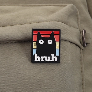Close-up of rectangular black cat enamel pin with bruh text on a green backpack