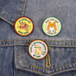 Set di tre spille smaltate con simpatici cani e slogan posizionate su giacca di jeans