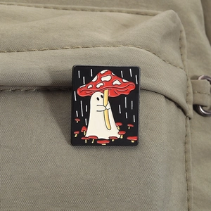Detail shot of a cute ghost mushroom enamel pin attached to a green canvas backpack