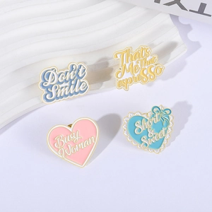 Set of four pastel enamel heart brooches with creative letter designs on white background
