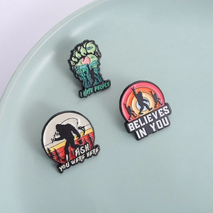 Three Bigfoot enamel pins with outdoor themes and quotes in a decorative ceramic tray