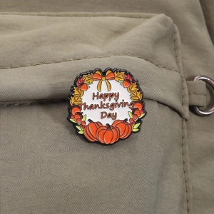 Detail of a Thanksgiving enamel pin with pumpkin and maple leaf on canvas bag