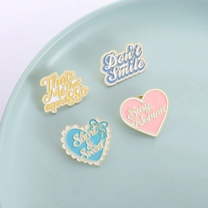 Set of four pastel enamel lapel pins with trendy English quotes on a ceramic tray