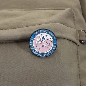 Detail einer Emaille-Anstecknadel mit Katze auf einem olivgrünen Rucksack in Nahaufnahme