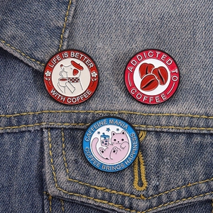 Tre spille smaltate a tema caffè con motivi di gatti e cani su tessuto denim blu