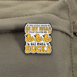 Detail of enamel pin with ducks and humorous text on olive green fabric background