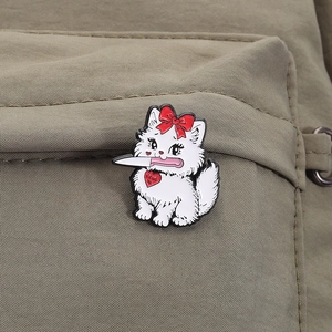 Close-up of a white cat enamel pin with a knife and red bow on a canvas bag