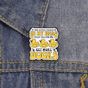 Detail of enamel pin with yellow ducks and text on blue denim fabric background