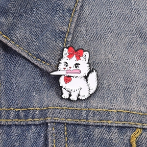 Spilla in smalto gatto bianco con coltello e fiocco rosso su tessuto denim scuro