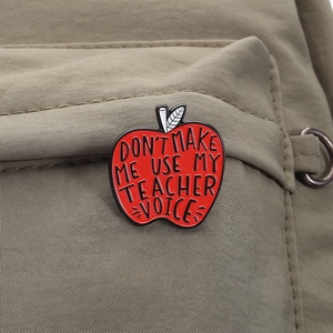 Detail of red apple enamel brooch pinned on green fabric with teacher quote text