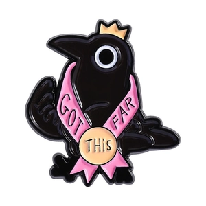 Cartoon crow enamel pin with golden crown and pink ribbon featuring motivational text