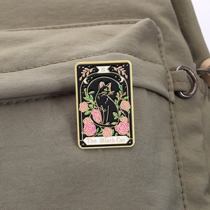 Detailed close-up of The Black Cat tarot enamel pin with pink roses on a green backpack