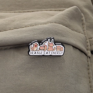 Detail of Orange Cat Energy enamel pin styled on a green canvas bag zipper flap