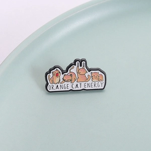 Creative orange cat enamel pin set with Orange Cat Energy text on a ceramic plate