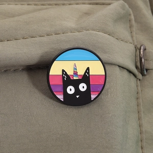 Detail of cute black cat unicorn enamel pin displayed on green canvas fabric texture