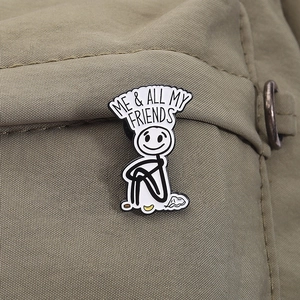 Detail of enamel pin with stick figure and ME & ALL MY FRIENDS text on green fabric