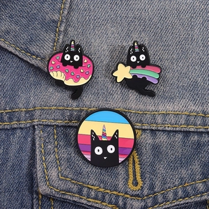 Detailed close-up of three enamel cat unicorn pins on blue denim fabric background
