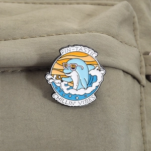Détail du pin's émaillé dauphin avec texte FIN-TASTIC sur un sac en toile verte
