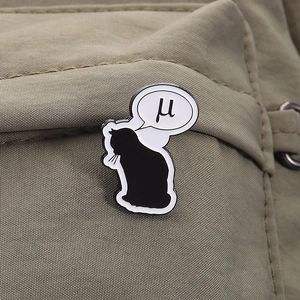 Détail d'un pin's chat noir avec bulle de texte 'μ' sur un sac en tissu beige texturé