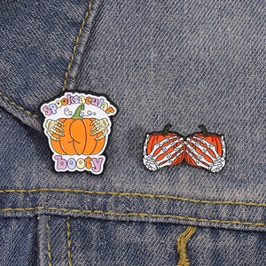 Detail of Halloween enamel pins with Spooktacular booty pumpkin and skeleton hand on denim