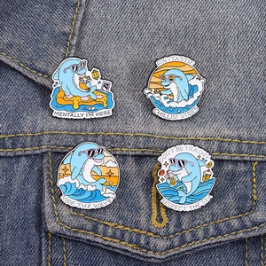 Set of four cartoon dolphin enamel pins on denim jacket featuring Ride The Wave text