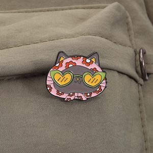 Detail of cute grey cat enamel pin with pink floral headscarf and green heart sunglasses