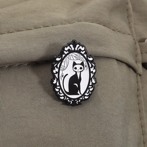 Close-up of a gothic black cat enamel brooch with spider web design on green fabric
