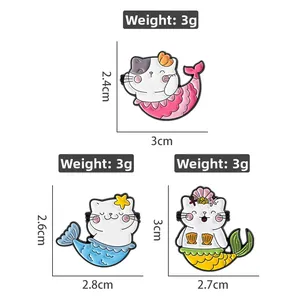 Détail de trois broches chat sirène en émail coloré avec décors de coquillages marins