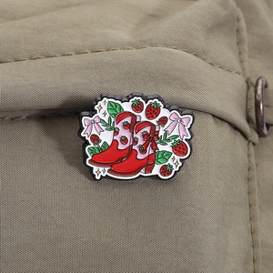 Gros plan détaillé d'une broche en émail botte de cowboy fraise sur toile de jute