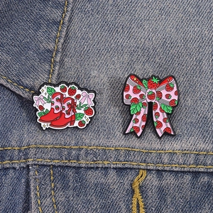 Broches émaillées bottes fraises et nœud rose sur fond de tissu en denim bleu