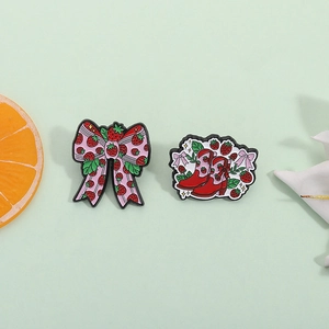 Lot de pin's en émail avec nœud fraise et botte rouge sur un fond décoratif vert clair